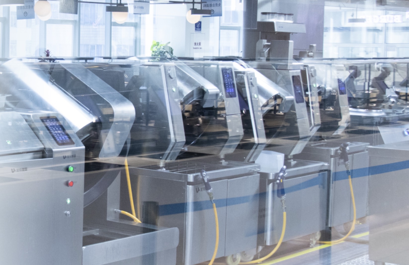 A row of automatic cooking robots in a commercial kitchen